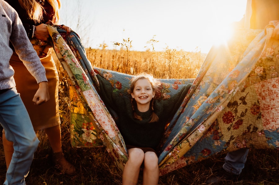 Little girl with blonde hair swinging on quilt at sunset
