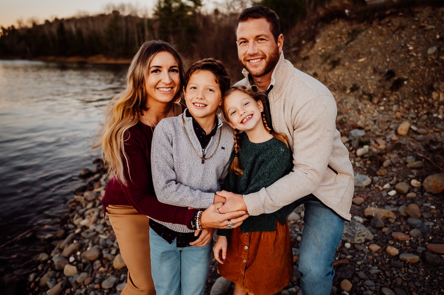 Family of four hugging in front of river bank