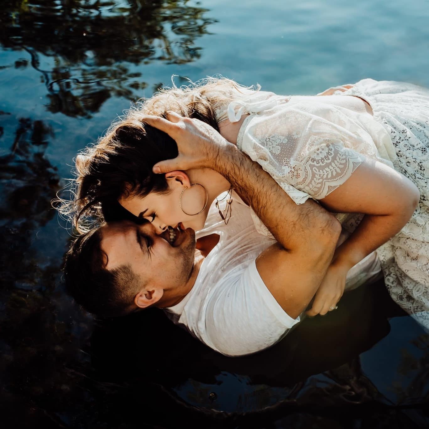 woman wearing white lace dress laying on man in water